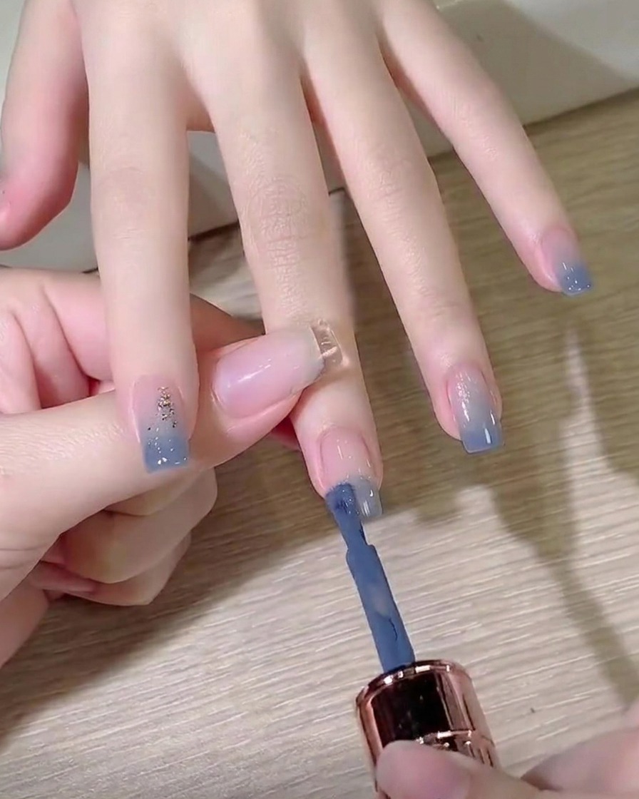 Un pincel de esmalte en gel aplicando color azul tiza en la punta de una uña preparada.