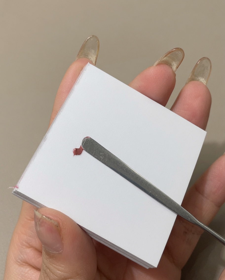 Una espátula metálica alisando una línea de esmalte en gel de color sobre la superficie de una paleta.