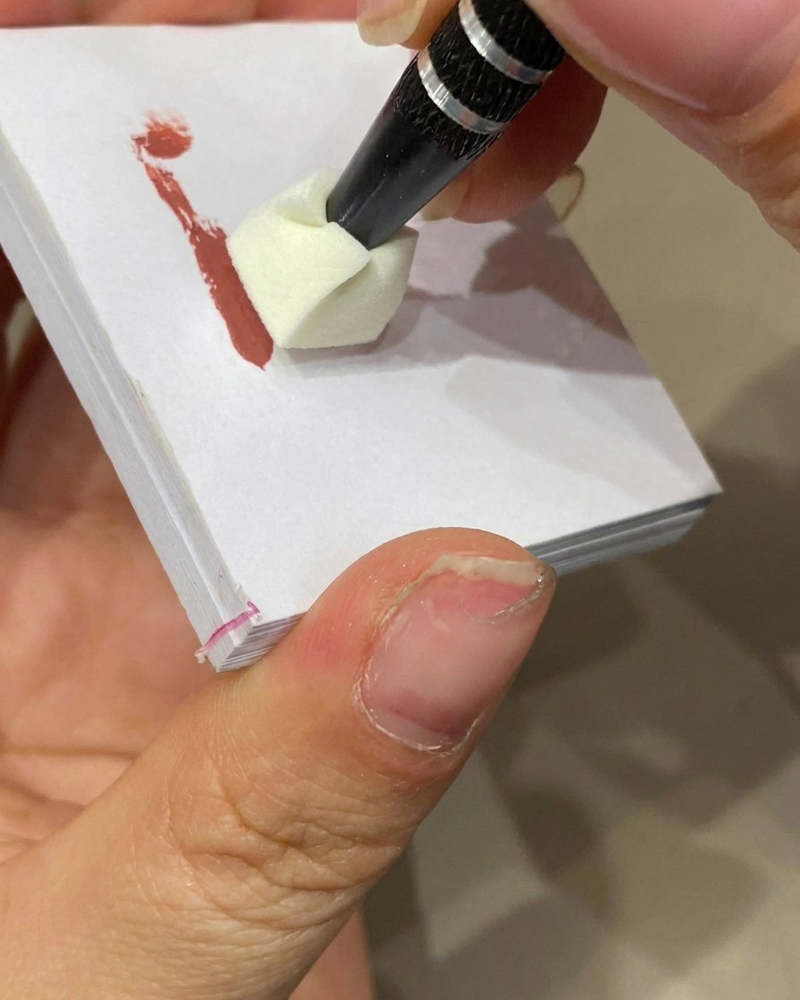Una esponja de maquillaje estampando gel de color sobre la punta de una uña con base nude para crear un efecto ombré.