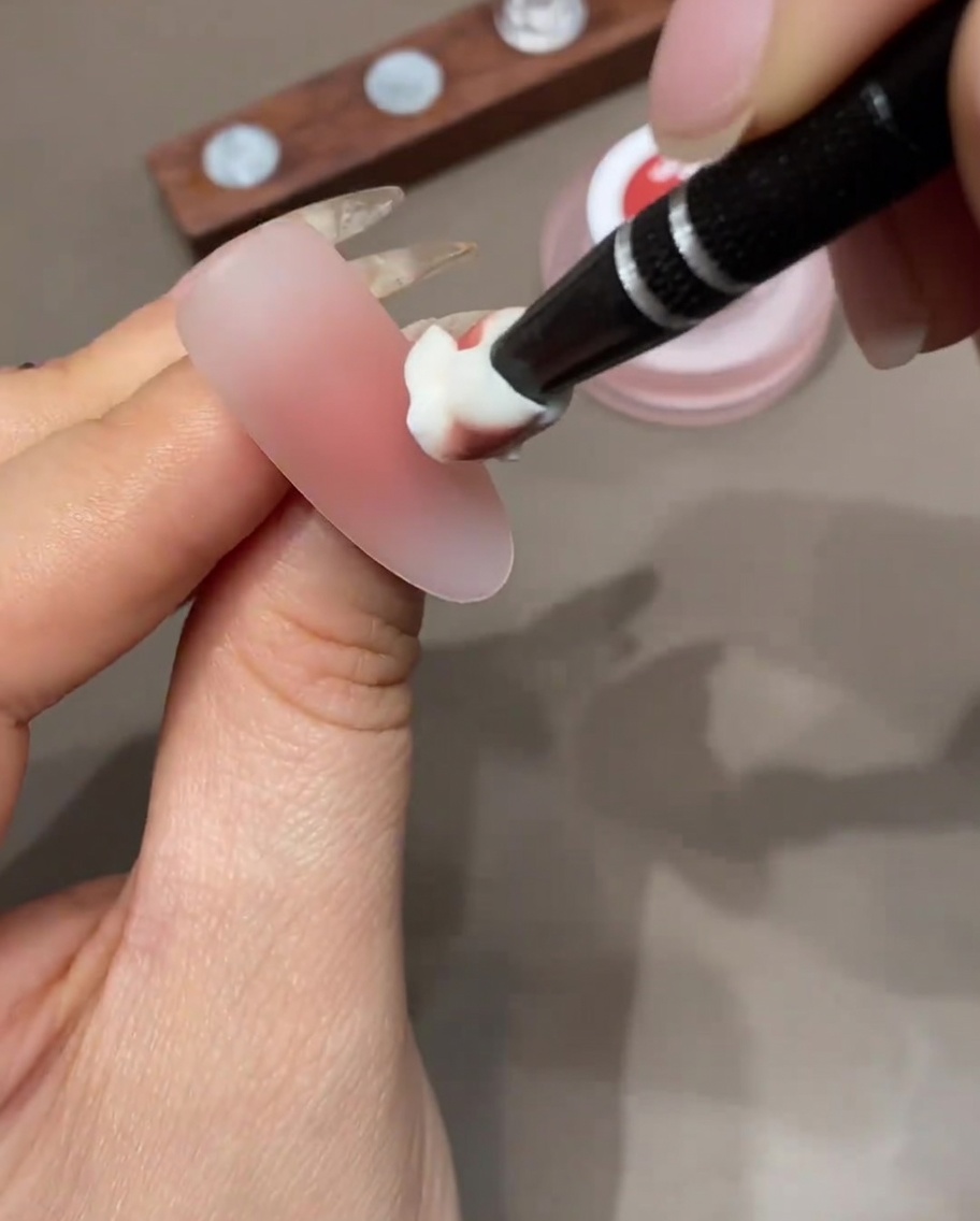 Una esponja de maquillaje aplicando una capa de esmalte en gel de color a la punta de una uña para construir un degradado ombré.