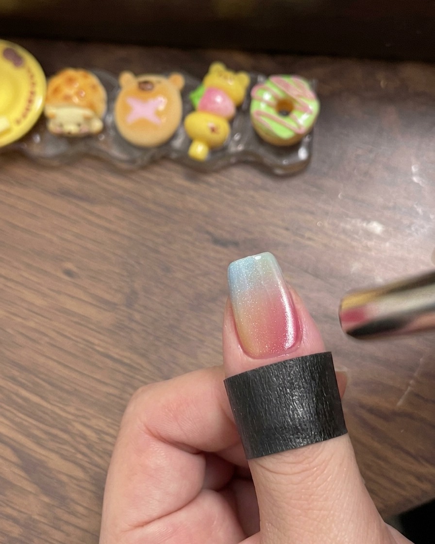 Un pincel aplicando top coat transparente y brillante sobre la uña con degradado multicolor.