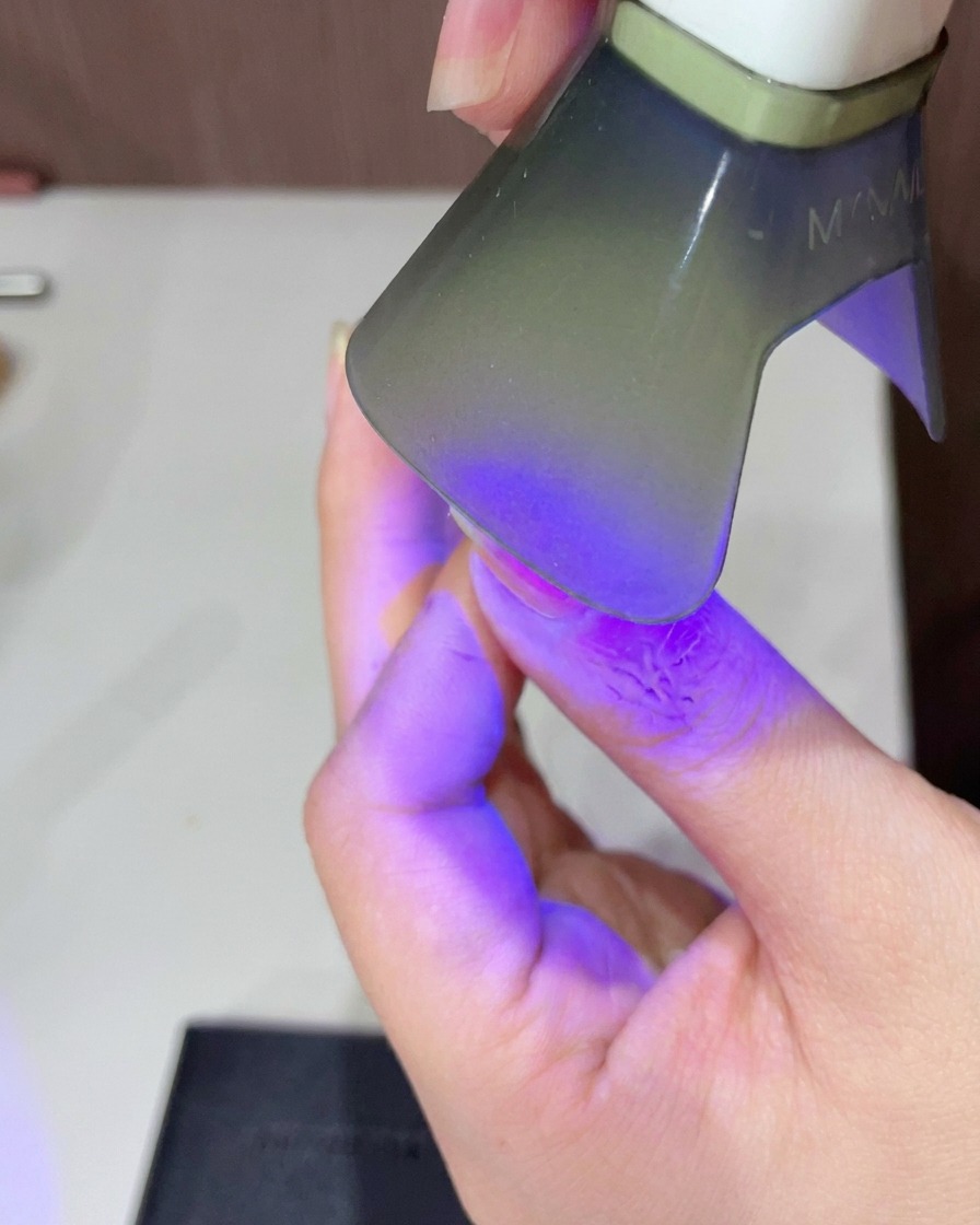 Primer plano de un dedo bajo una pequeña lámpara UV LED portátil curando el top coat brillante.