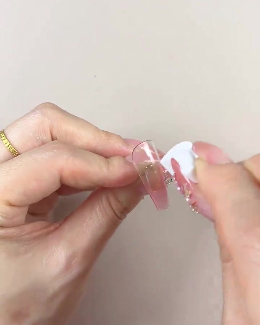Una mano usando una sección limpia de una esponja cosmética para suavizar y refinar el degradado de color en un tip de uña.