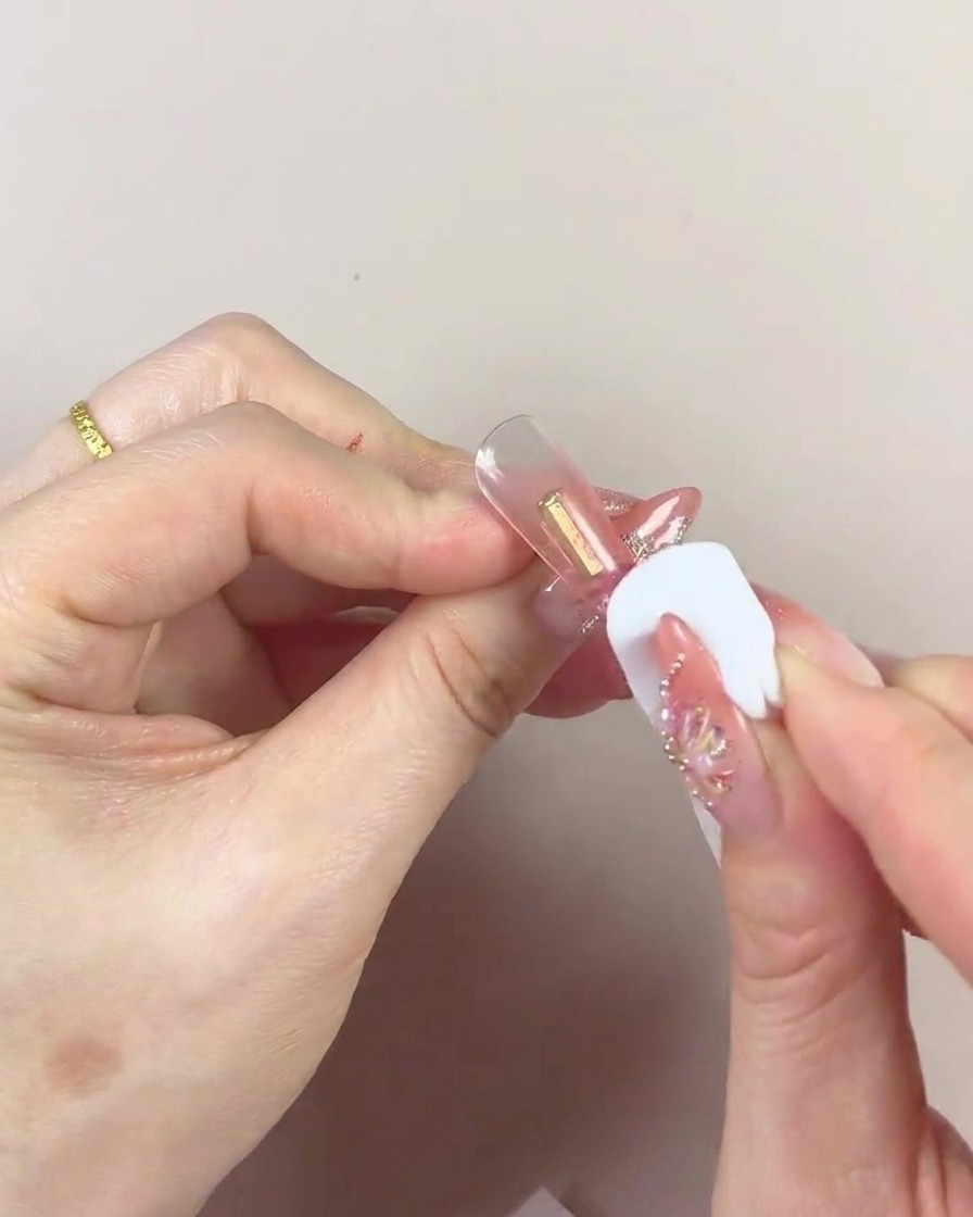 Primer plano de una esponja cosmética con el centro oscuro siendo utilizada para aplicar gel en un tip de uña.