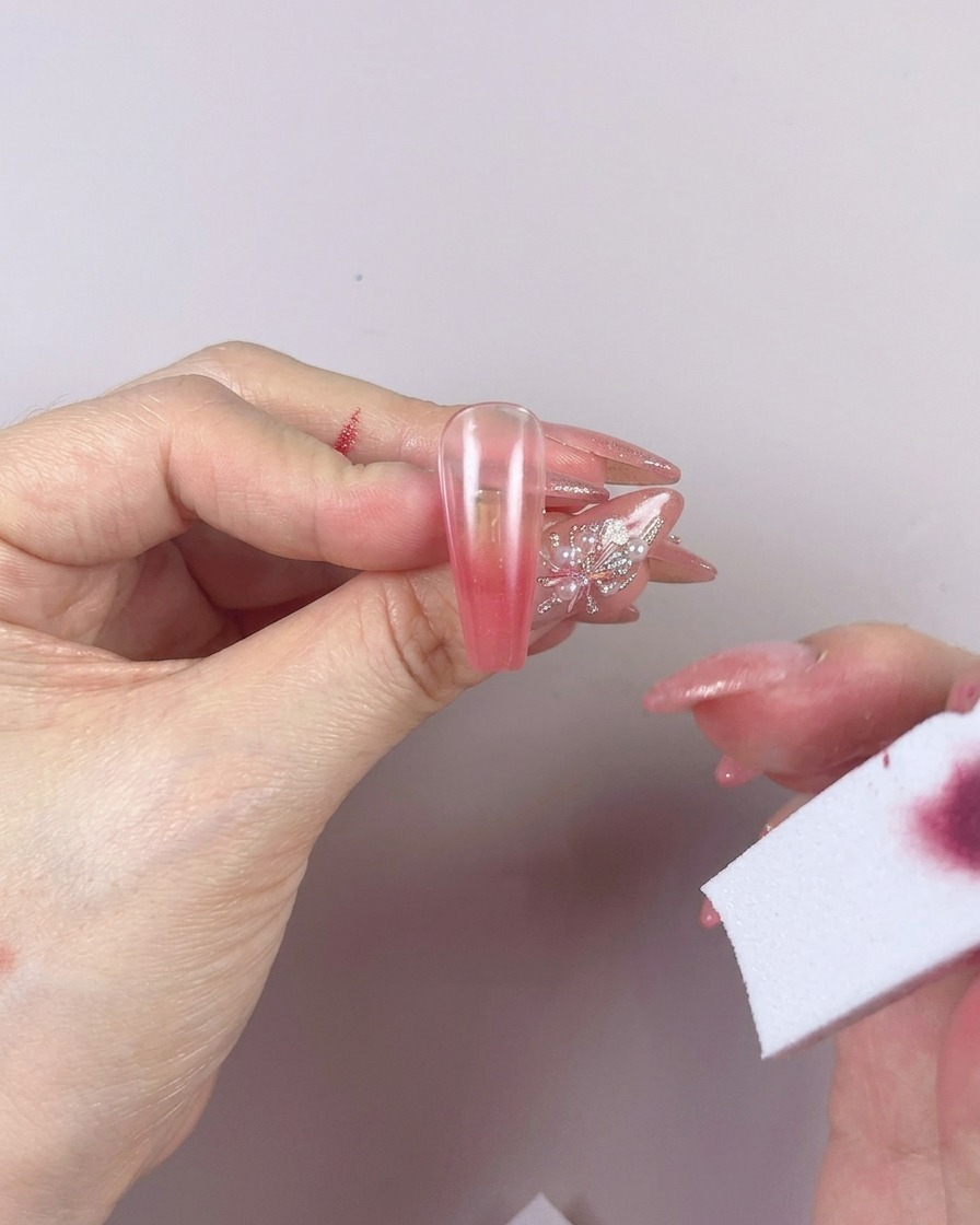Una esponja siendo utilizada para difuminar el color del gel en una uña con movimientos horizontales de izquierda a derecha.