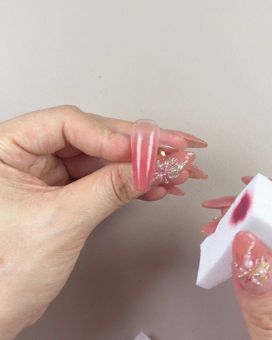 Primer plano de una mano usando una esponja de maquillaje para difuminar suavemente el degradado en una uña.