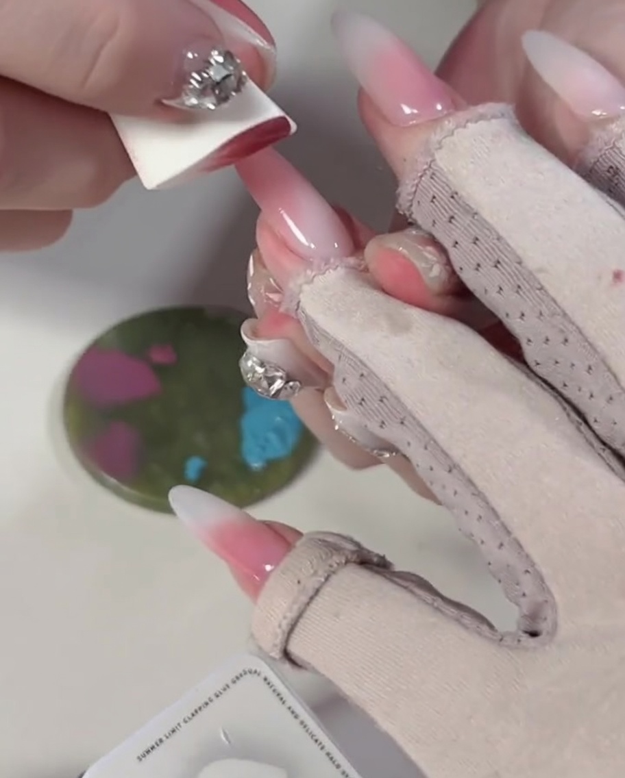 Primer plano de una esponja presionando sobre bloques de esmalte de gel azul y rosa en una paleta de mezcla.