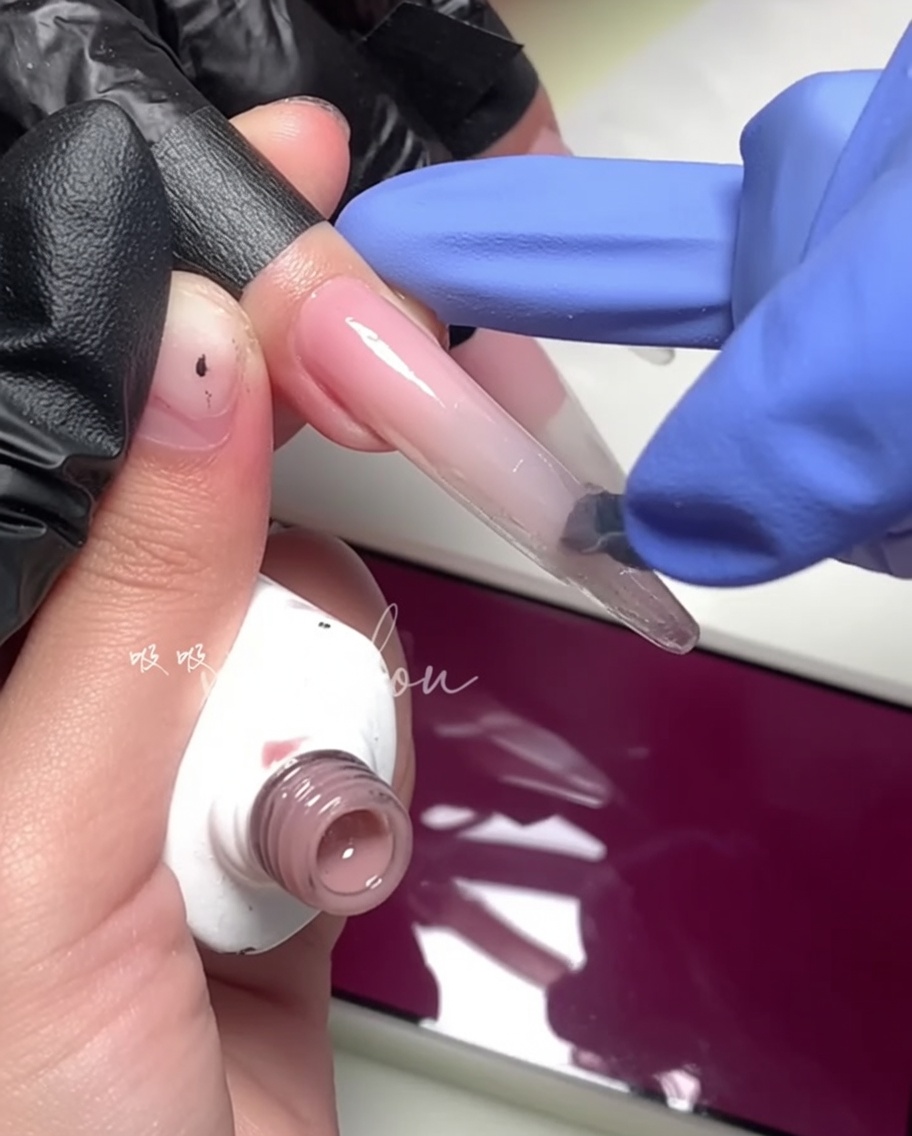 Primer plano de un pincel aplicando un gel magenta brillante en la mitad exterior de la uña.