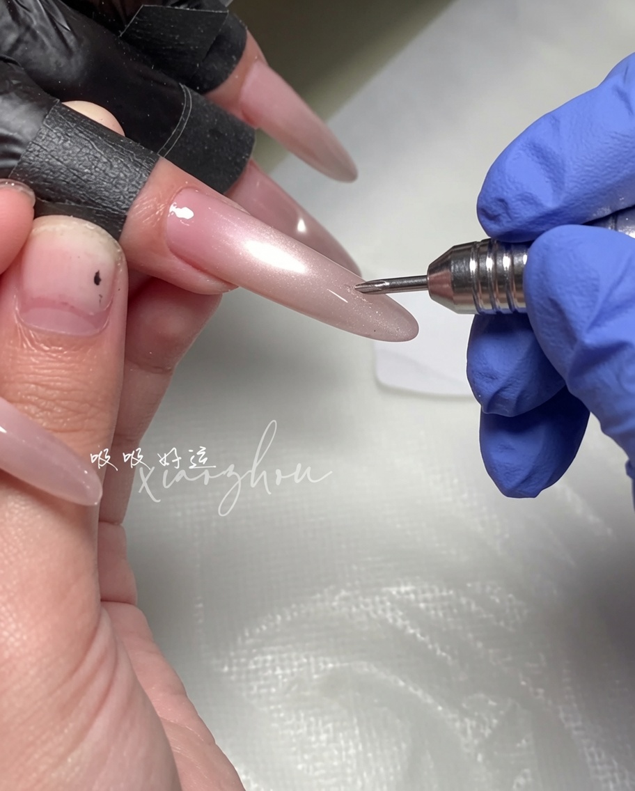 Una mano sosteniendo una varita magnética sobre una uña larga en forma de almendra con gel de ojo de gato magenta húmedo.