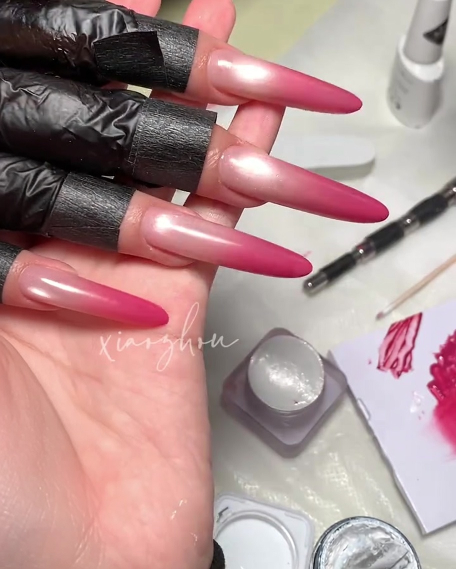 Un pincel aplicando un top coat transparente y brillante sobre un diseño de uñas de gel magnético magenta.