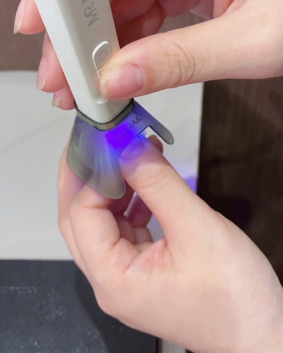 Primer plano de un pequeño punto de esmalte de gel amarillo vibrante aplicado en el centro de la uña con punta magenta.