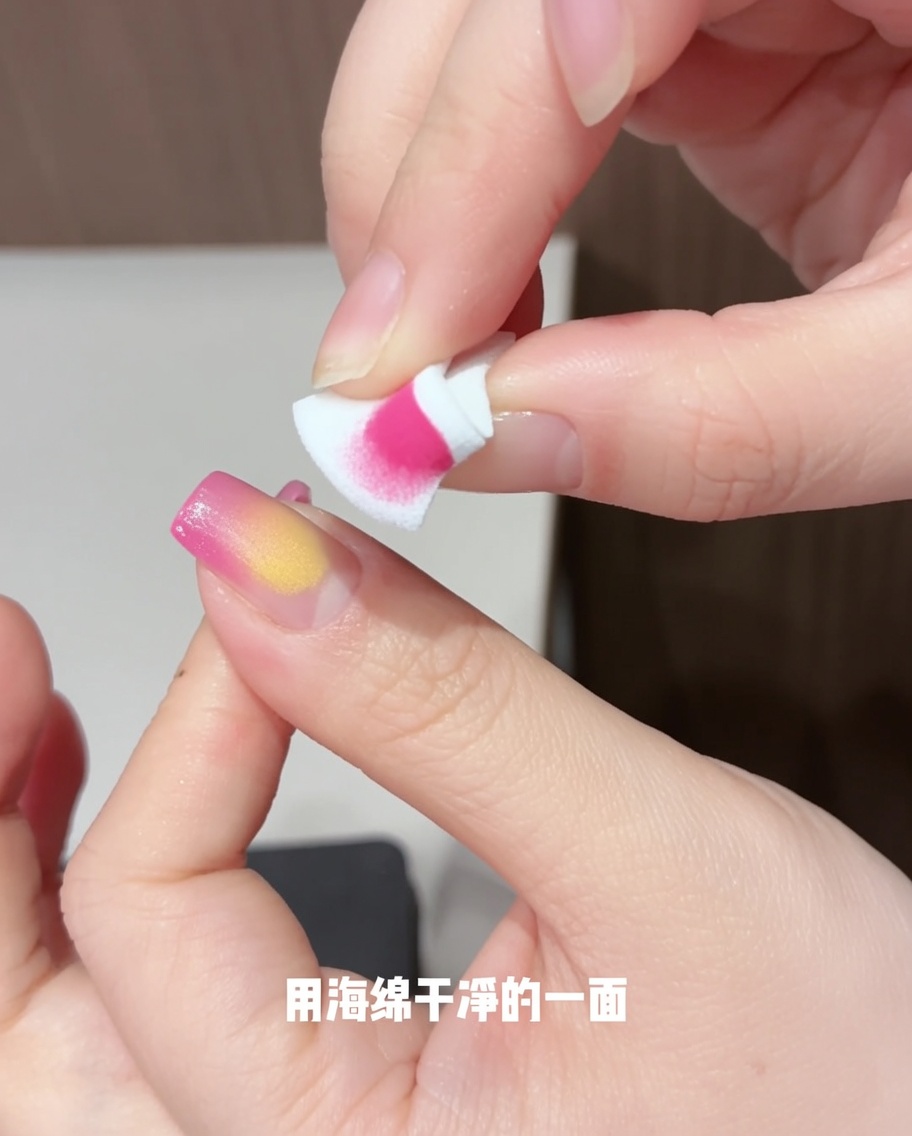 Una esponja siendo utilizada para dar toques y expandir el gel amarillo sobre la uña creando una forma de pétalo difuminado.