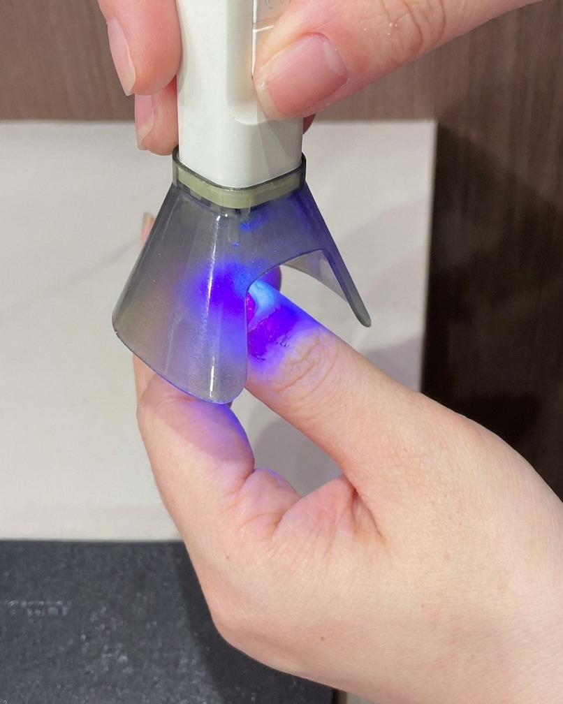 Un dedo siendo sostenido bajo una lámpara UV portátil para el paso de endurecimiento final de la manicura.