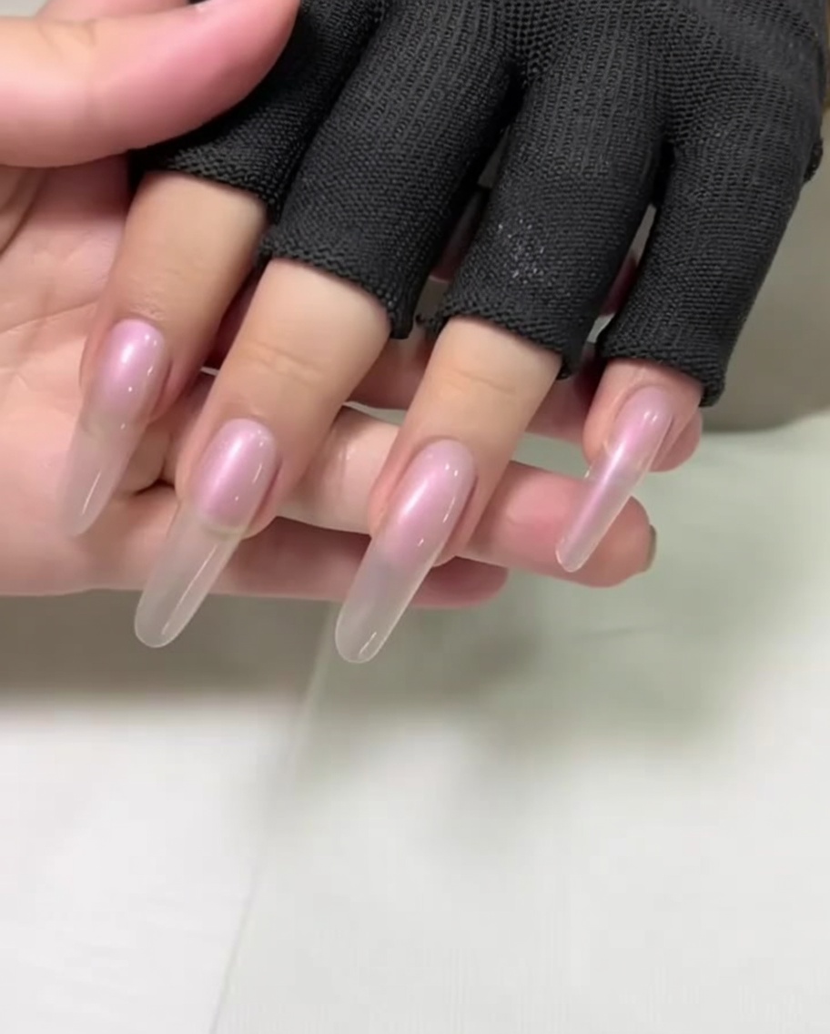 Primer plano de una mano con uñas largas almendradas siendo preparadas empujando las cutículas con un empujador de metal.