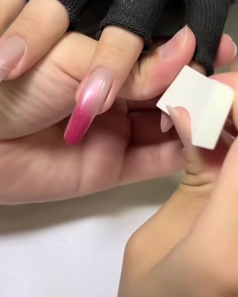 Mano sosteniendo una esponja de maquillaje blanca aplicando un color rosa claro en la parte superior de una uña almendrada.