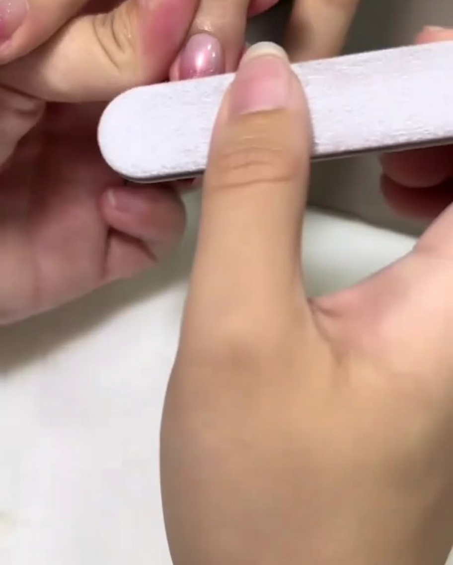 Mano sosteniendo una lima puliendo suavemente el centro de una uña esmaltada en tono rosa.