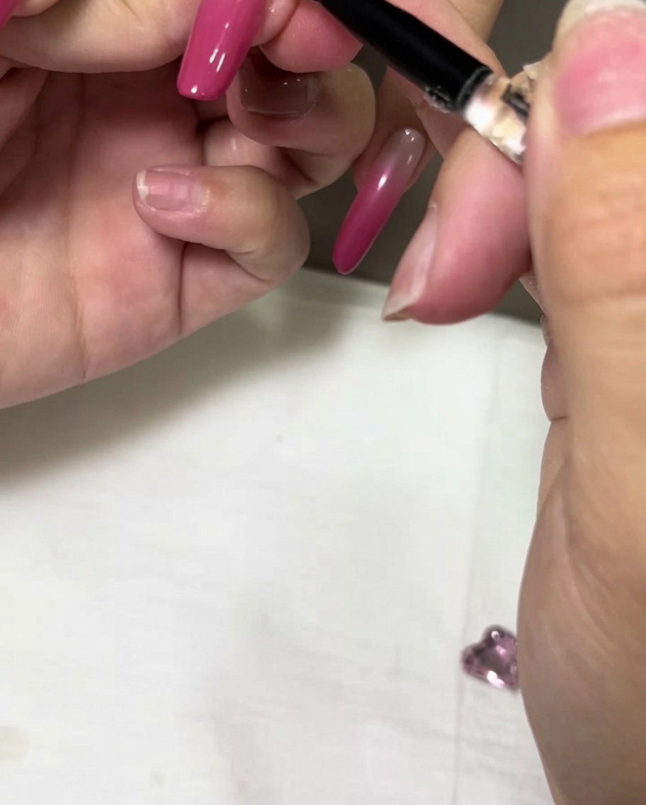 Pincel de detalles aplicando una gota de gel adhesivo transparente sobre una uña rosa ombré.