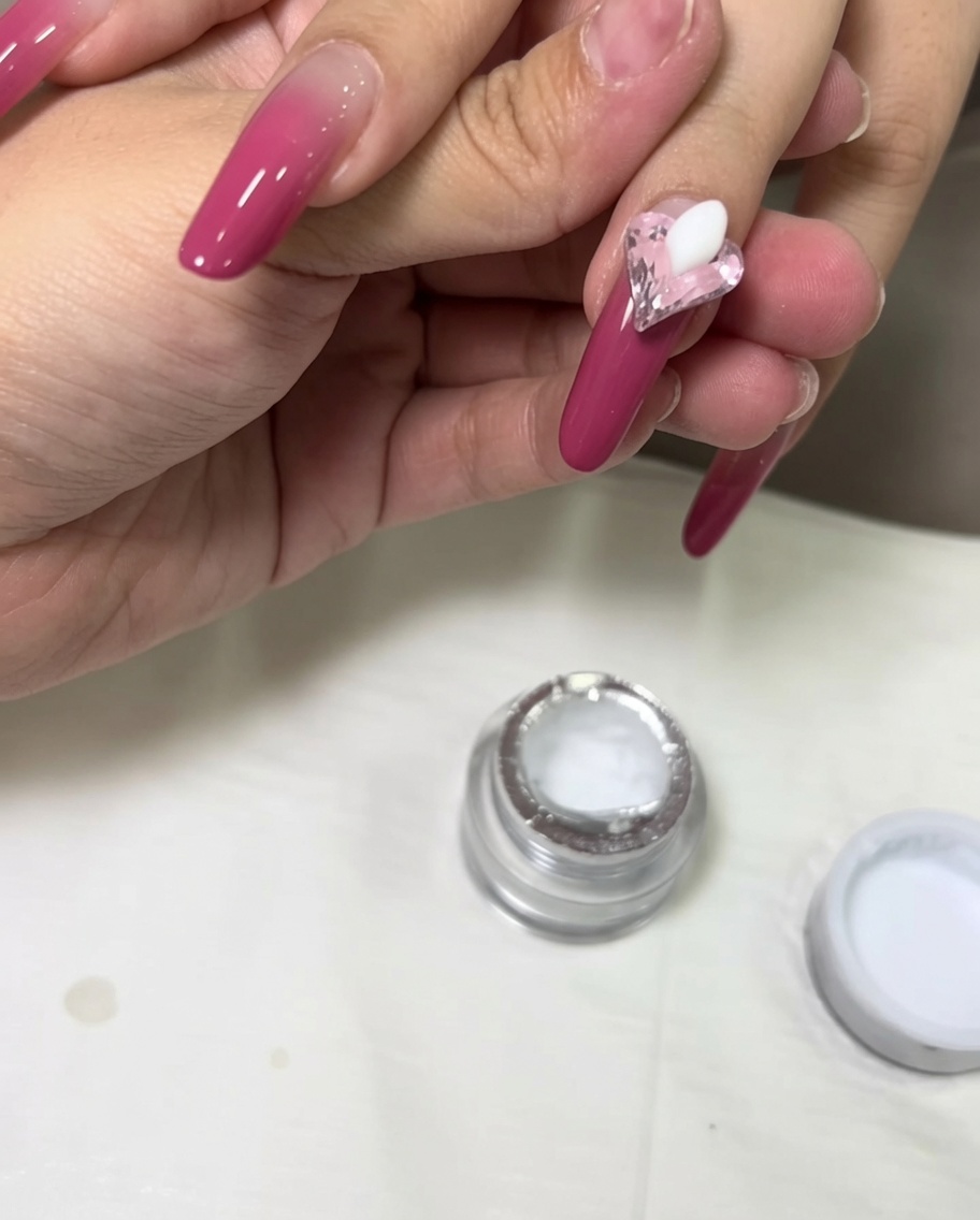 Gota de gel de esculpir blanco 3D colocada en la uña junto a un cristal rosa de corazón.