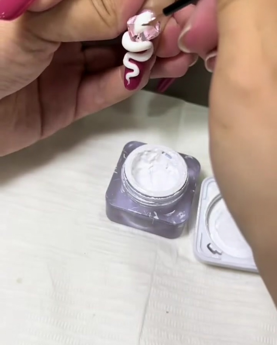 Pincel delineador fino aplicando gel blanco para añadir textura al diseño de una serpiente 3D en una uña.