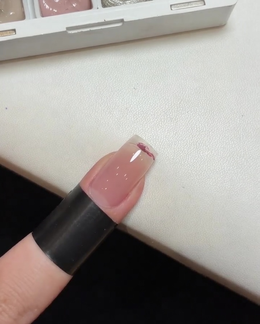 Uso de una esponja para dar pequeños toques y difuminar el esmalte en gel rosa sobre la uña, creando un efecto degradado.