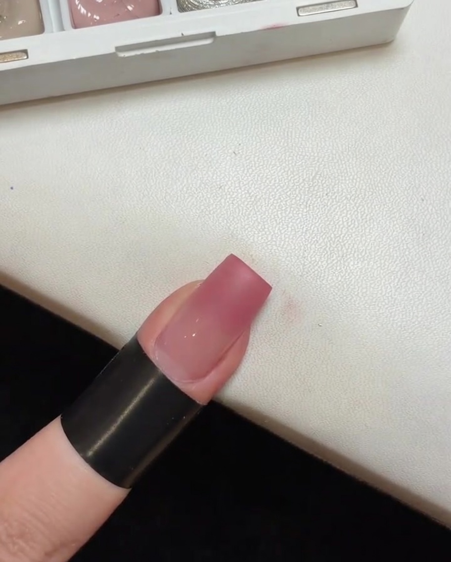 Una uña con una base degradada en tono rosa curándose dentro de una pequeña lámpara UV portátil.