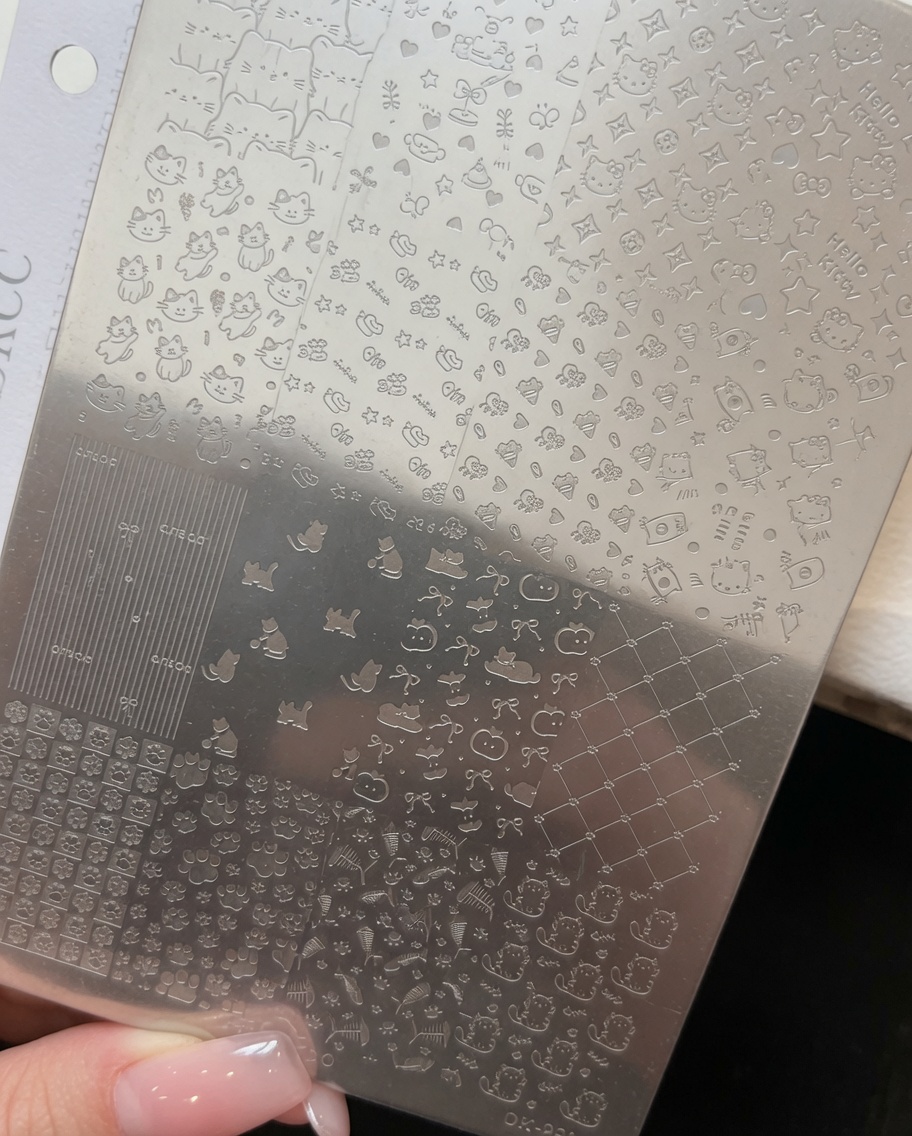 Aplicación de una fina capa de esmalte en gel color rosa empolvado sobre un diseño de Kitty en una placa de estampado de metal.