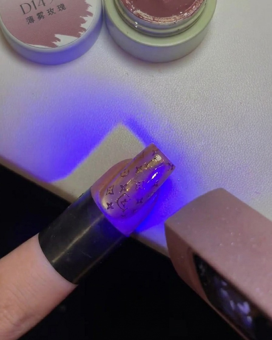 Un dedo con un diseño de Hello Kitty estampado en la uña bajo la luz violeta de una lámpara UV.