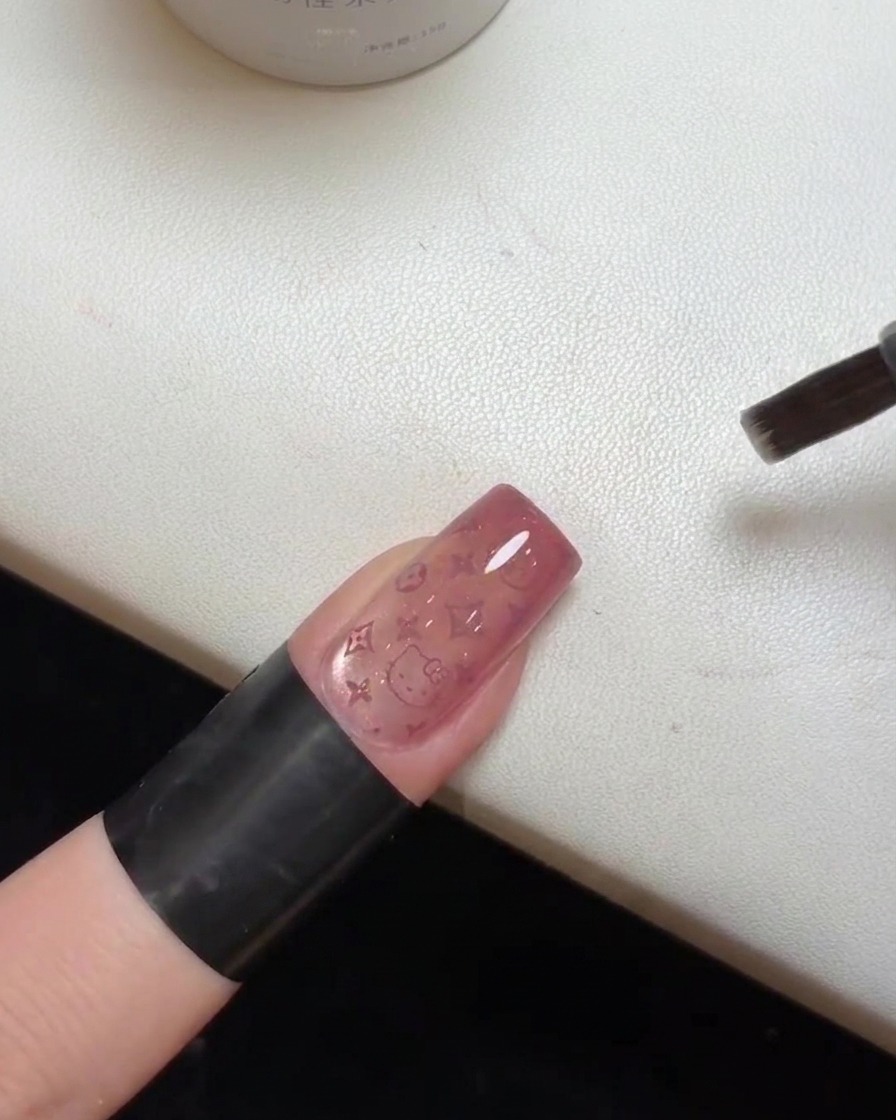 Primer plano de una uña terminada con el top coat curándose bajo una lámpara UV.