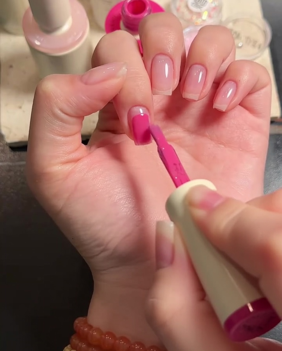Primer plano de un pincel plano aplicando gel rosa sobre la superficie de una uña.