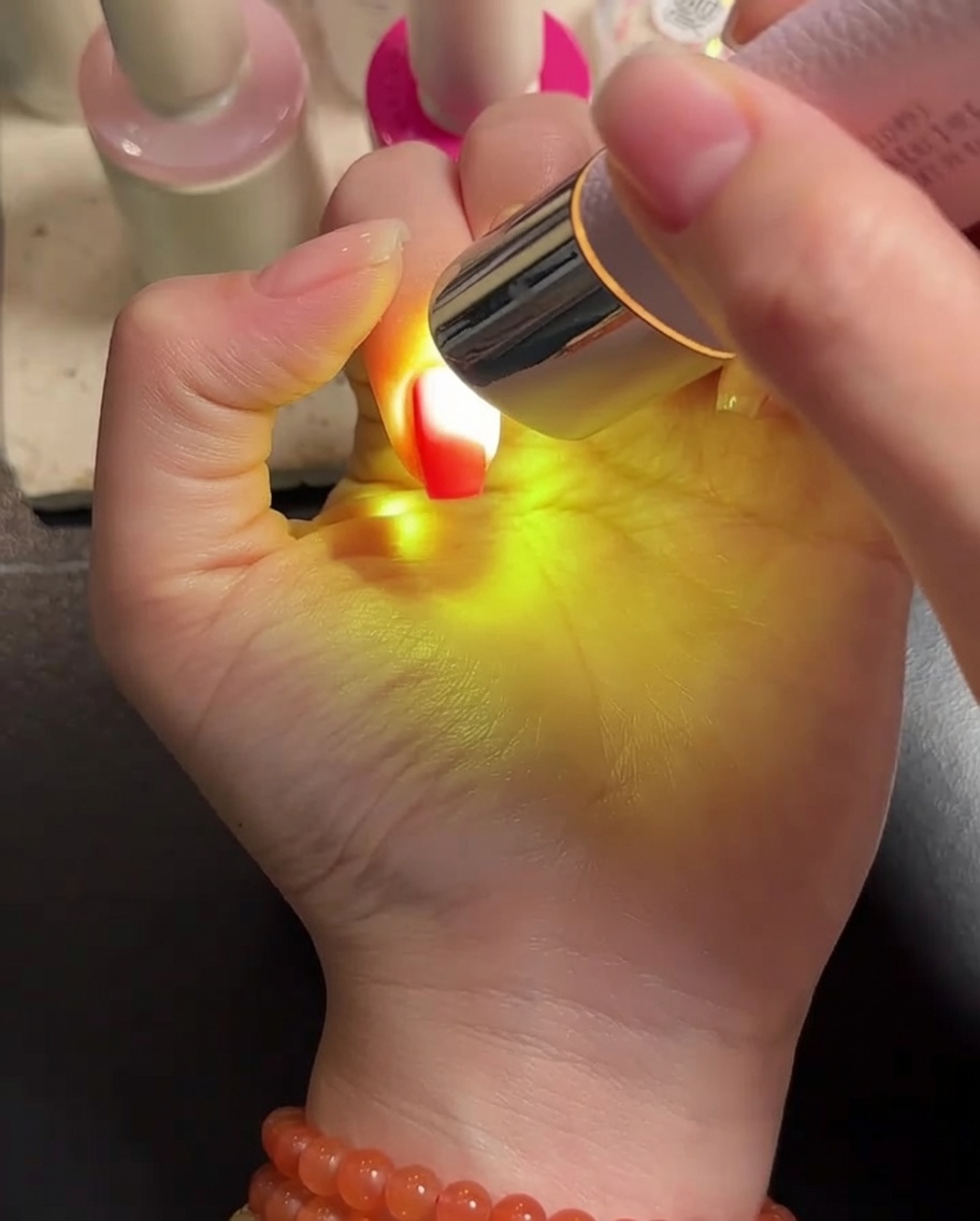 Una mano bajo una lámpara LED portátil, curando las uñas con gel.