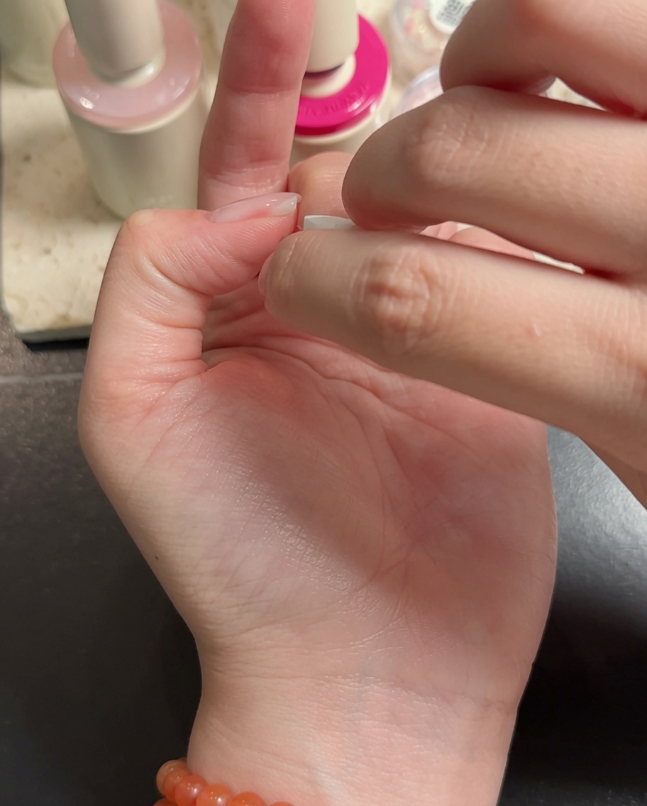Un pincel para nail art aplicando gel blanco en las puntas de los dedos medio y anular para crear un efecto ombré.