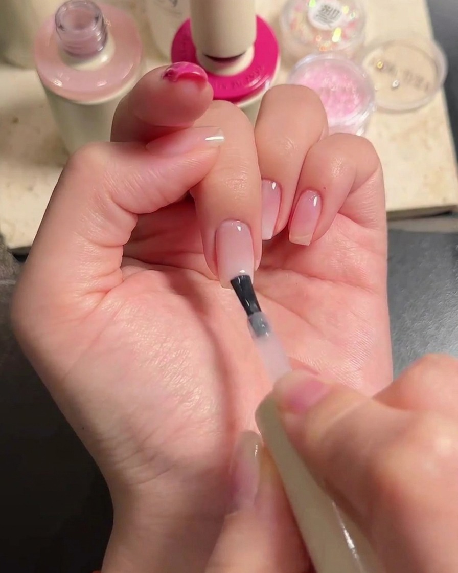 Un pincel aplicando gel nude traslúcido sobre los dedos medio y anular para integrar el degradado.