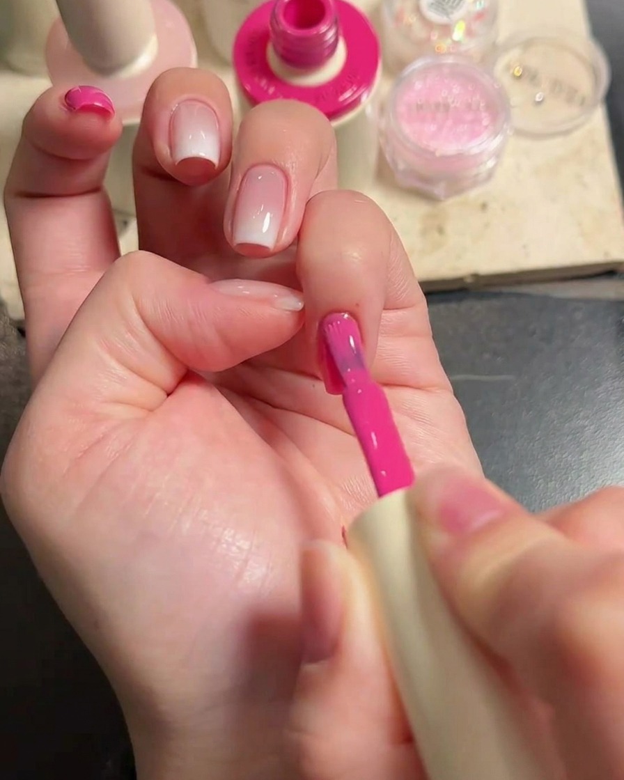 Primer plano de una mano con un pincel aplicando gel rosa vibrante en las uñas.
