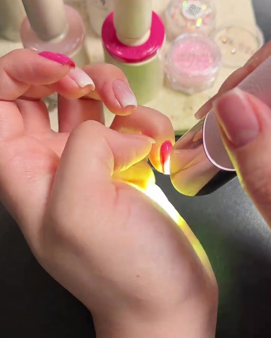 Un pincel aplicando top coat brillante sobre uñas manicuradas.