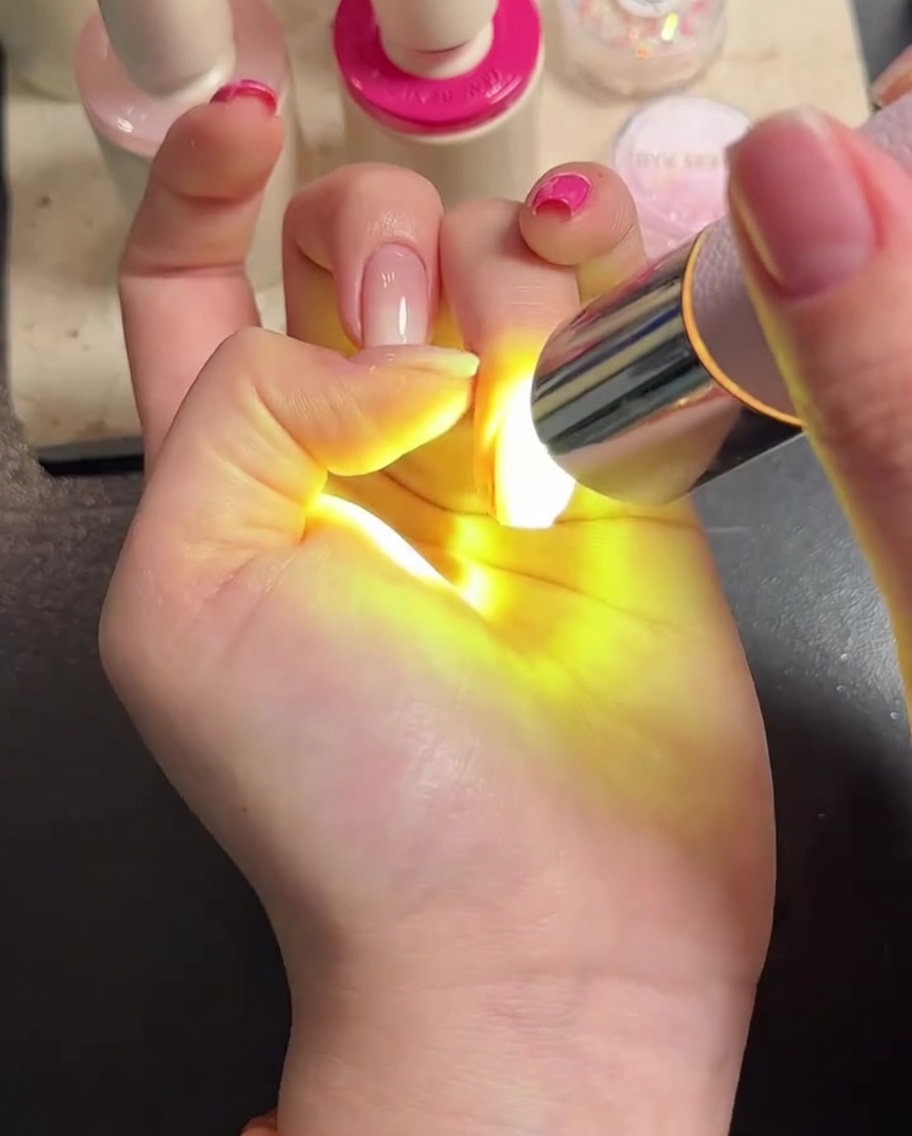 Una mano bajo una lámpara LED, curando el top coat.