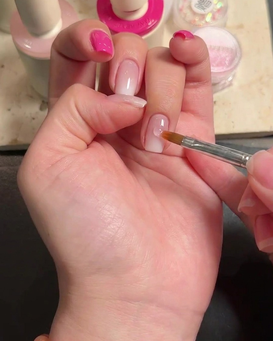 Primer plano de una gota de pegamento para uñas en el centro de la uña del dedo anular.