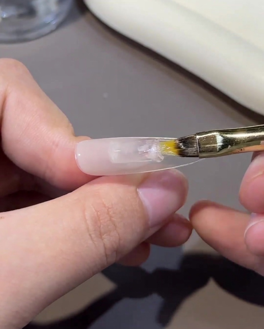 Una mano sosteniendo un tip de uña bajo el brillo de una lámpara UV/LED profesional.