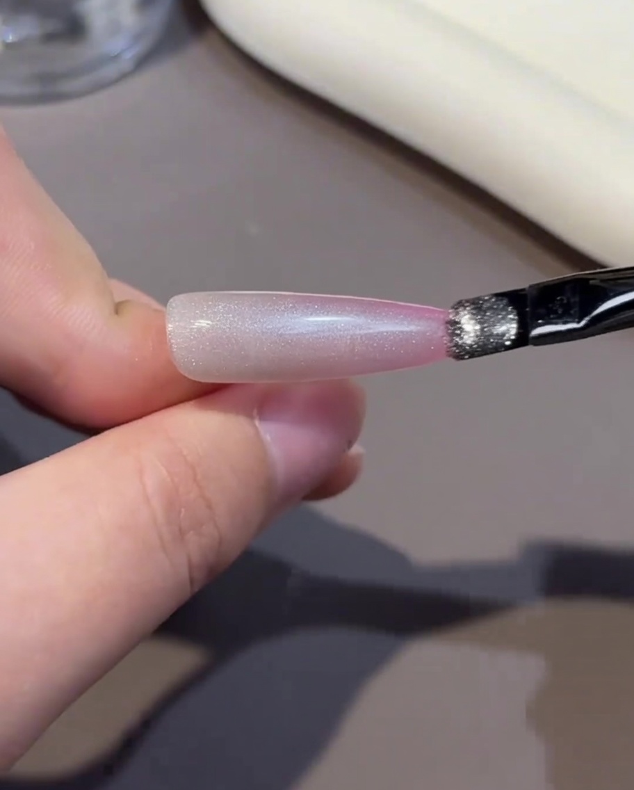 Un pincel aplicando una capa de esmalte de gel rosa en la punta de una uña.