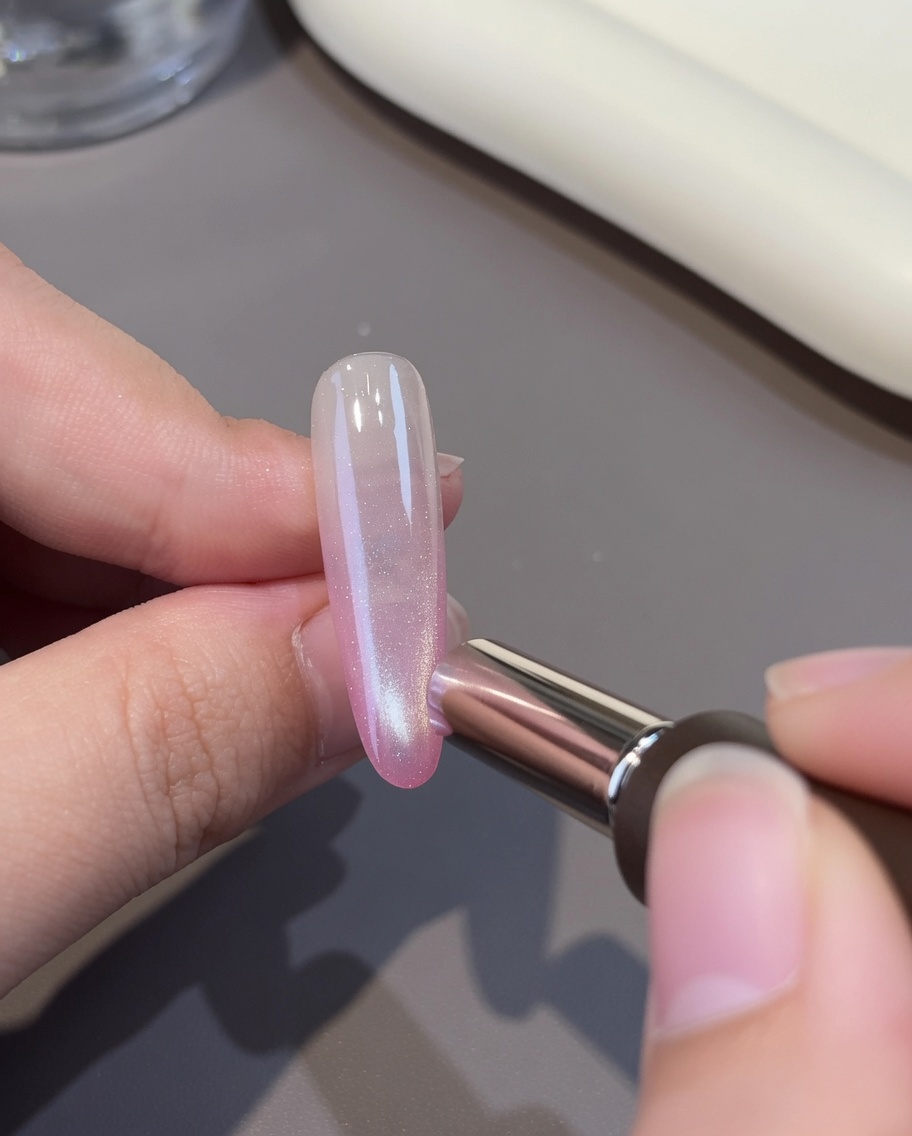 Una capa de gel cat-eye blanco siendo aplicada sobre la base rosa en una uña.