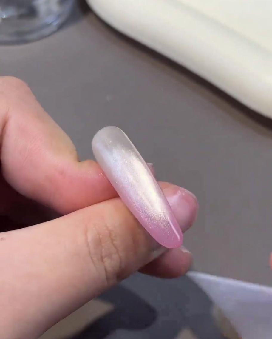 Un imán siendo sostenido cerca de una uña para manipular las partículas en el gel cat-eye húmedo.