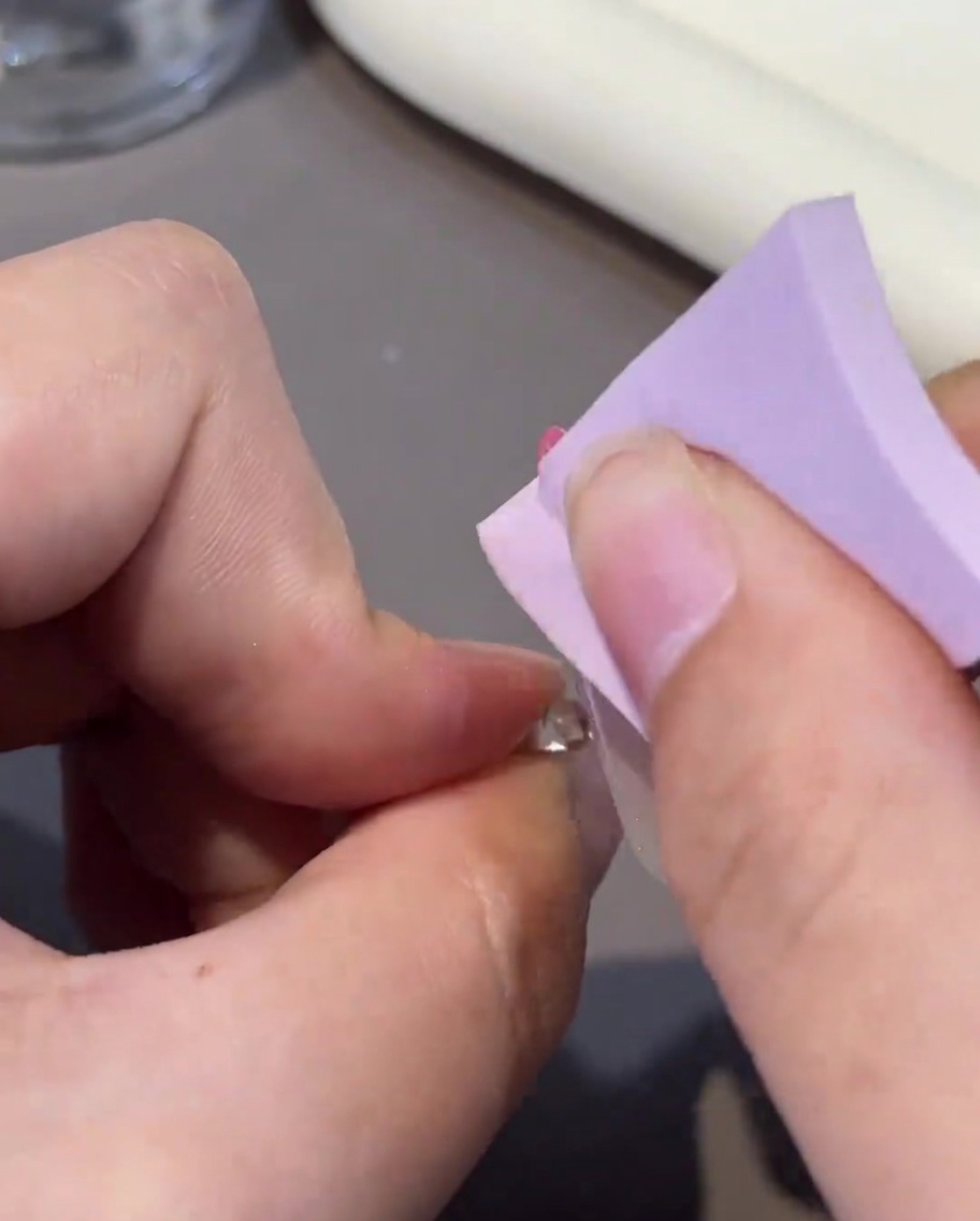 Una toallita sin pelusa siendo utilizada para limpiar la superficie de una uña de gel curada.