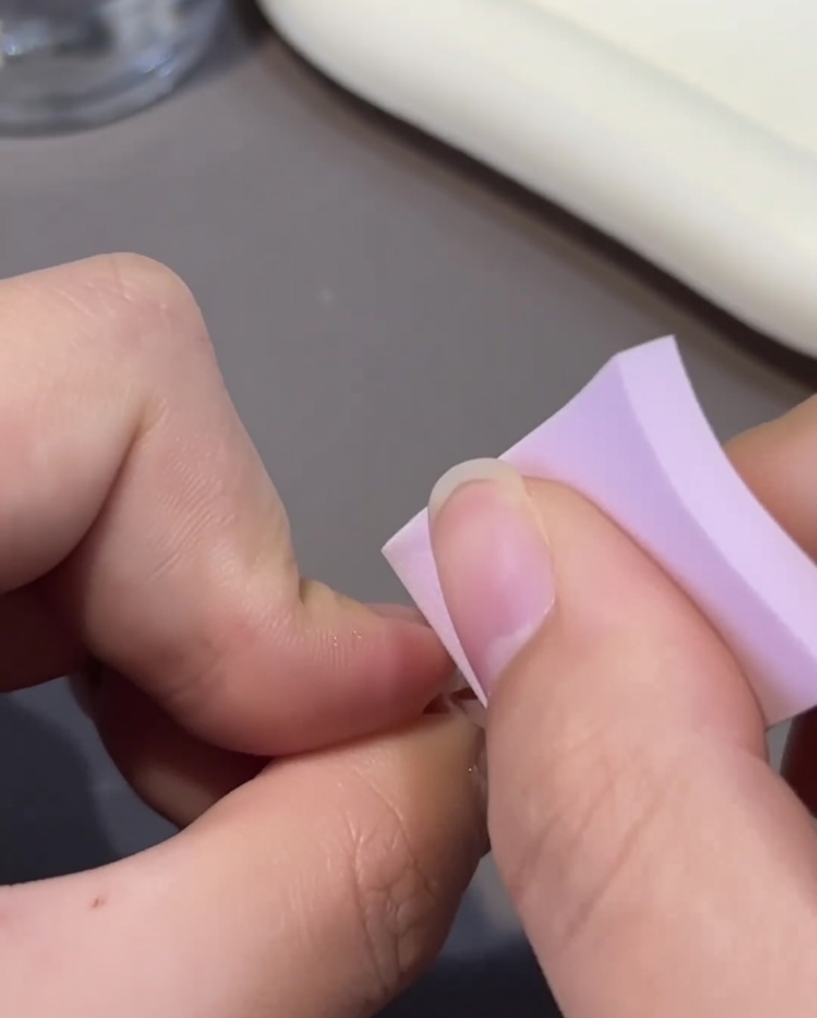 Vista en primer plano de una uña ombré rosa siendo recubierta con una segunda capa de esmalte de gel rosa usando un pincel pequeño.