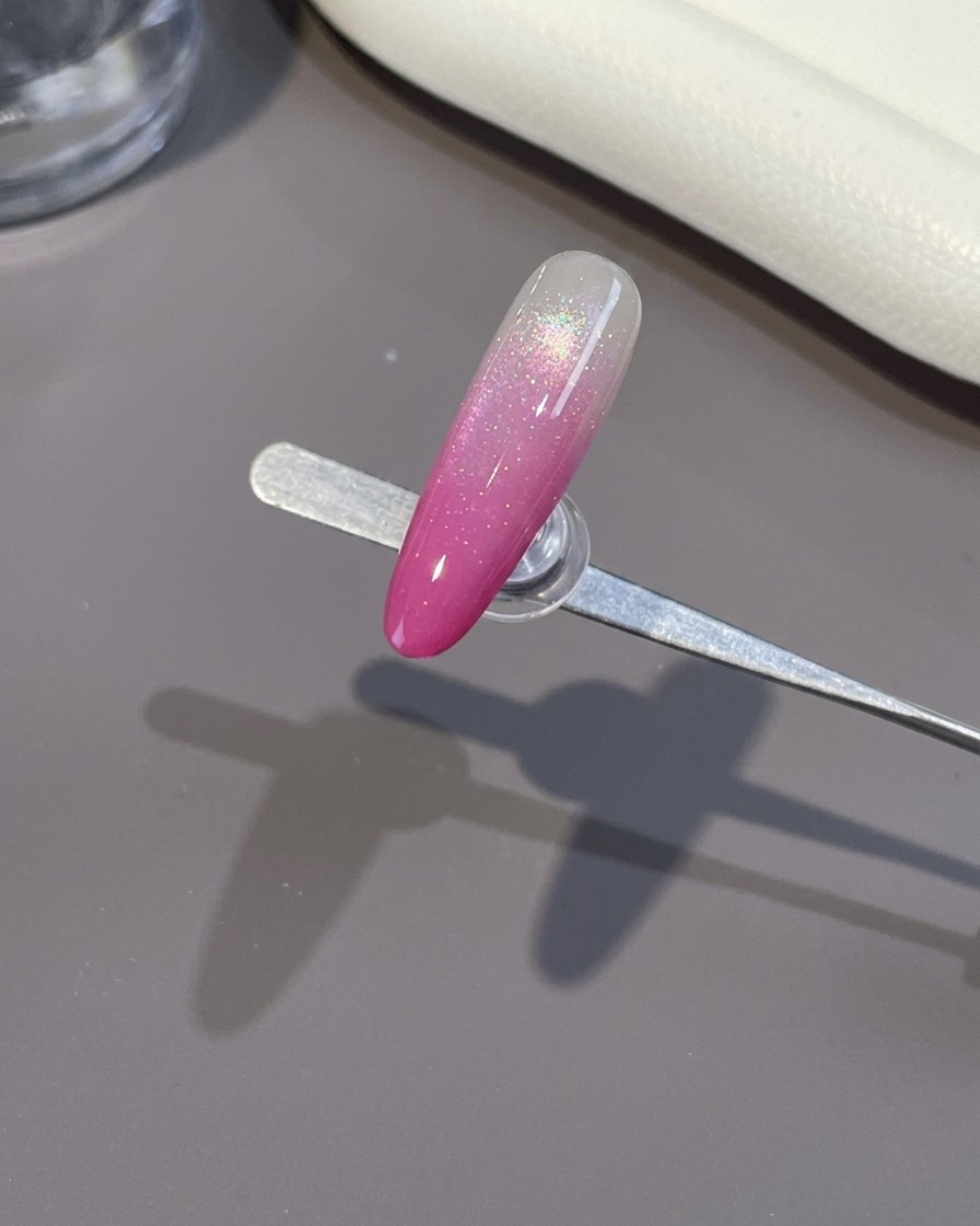 Un pincel aplicando un top coat transparente y brillante sobre una uña ombré rosa terminada.