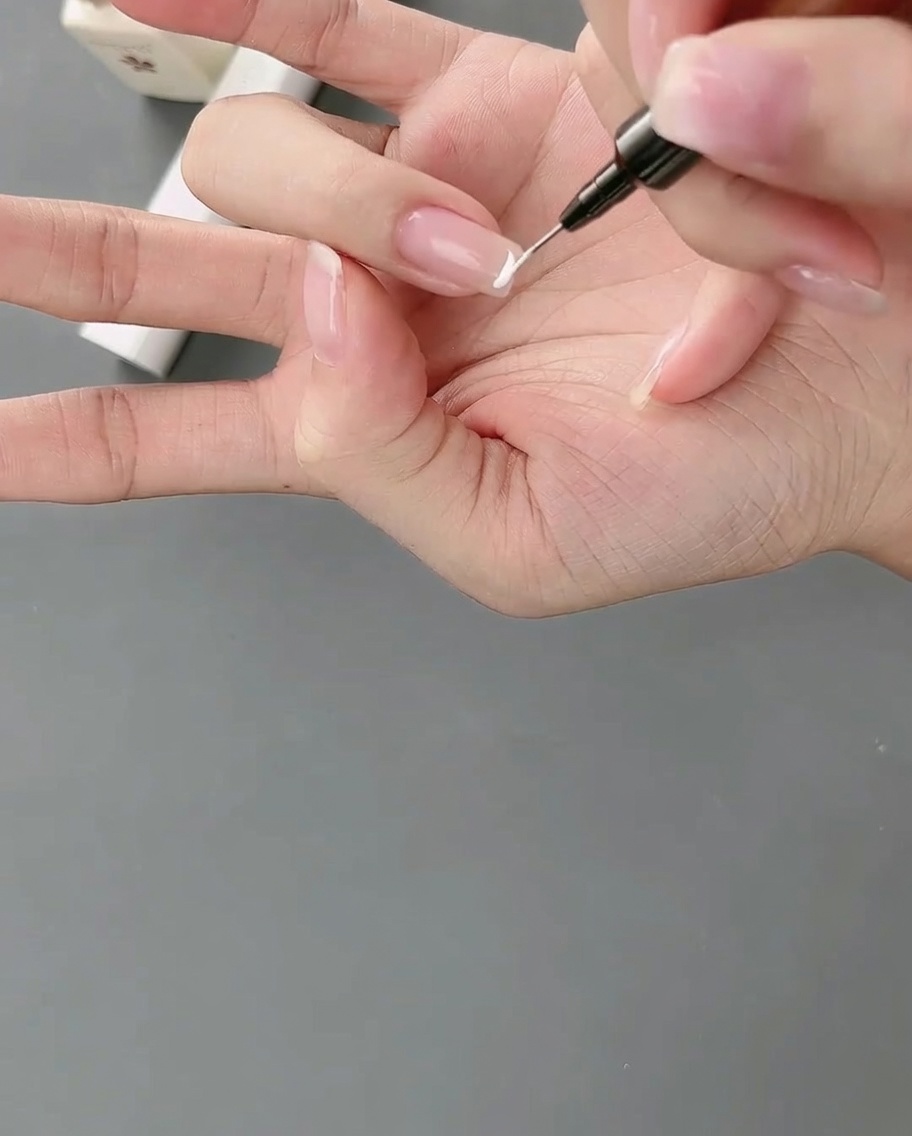 Un pincel liner aplicando una línea de gel blanco precisa para crear una punta francesa alta en una uña.