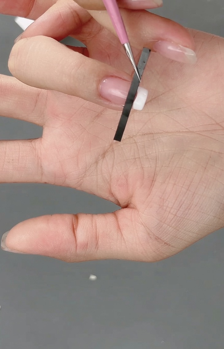 Primer plano de una pegatina de francesa siendo colocada en la punta de la uña para crear una guía de cuadrícula.
