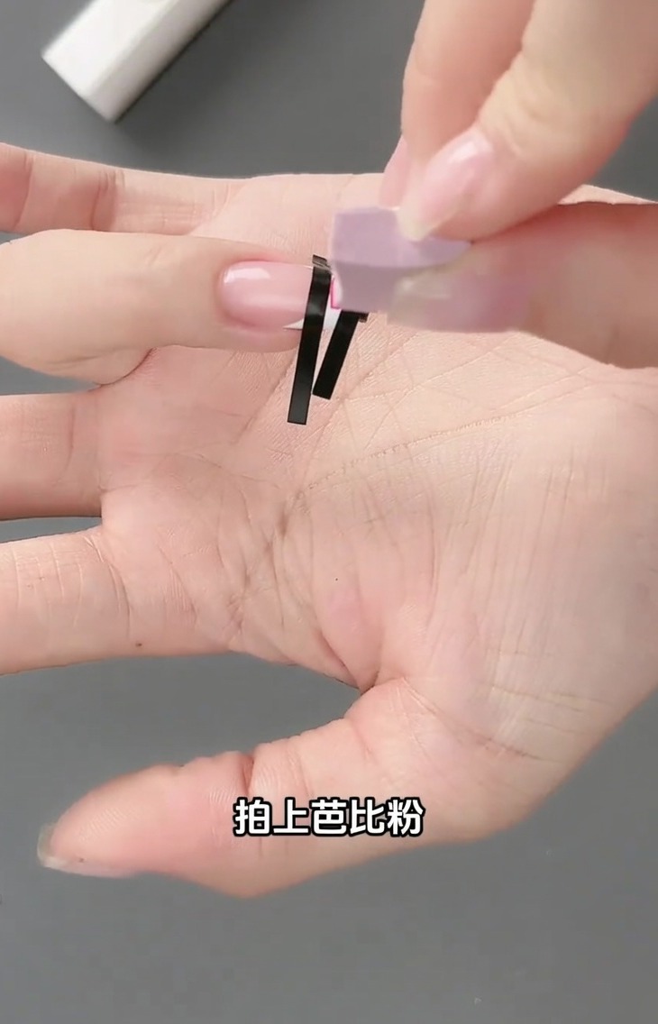 Una pequeña esponja aplicando gel rosa claro sobre la cuadrícula de la pegatina de francesa en una uña.