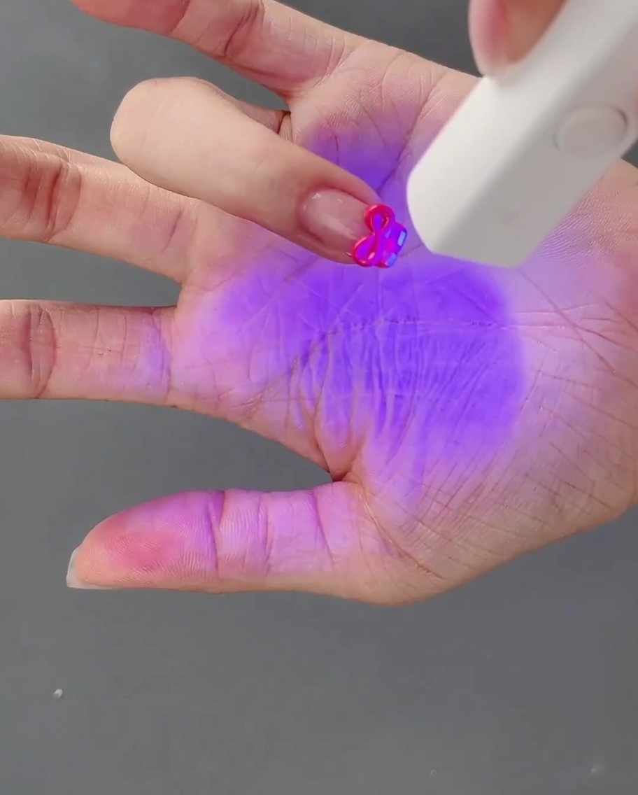 Una mano con un lazo de gel 3D recién esculpido siendo curado bajo una lámpara UV.