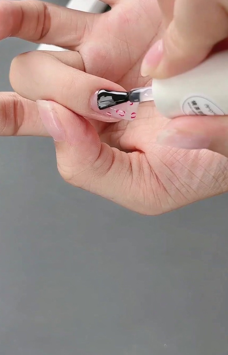Un pincel aplicando un top coat brillante sobre el diseño final de francesa y lazo 3D.