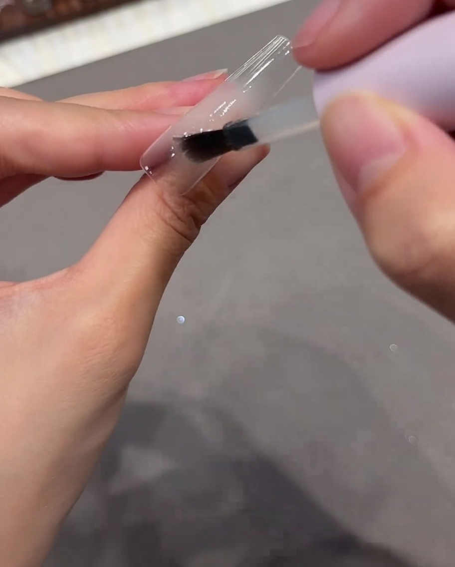 Un pincel aplicando una capa base de gel transparente sobre una punta de uña clara.