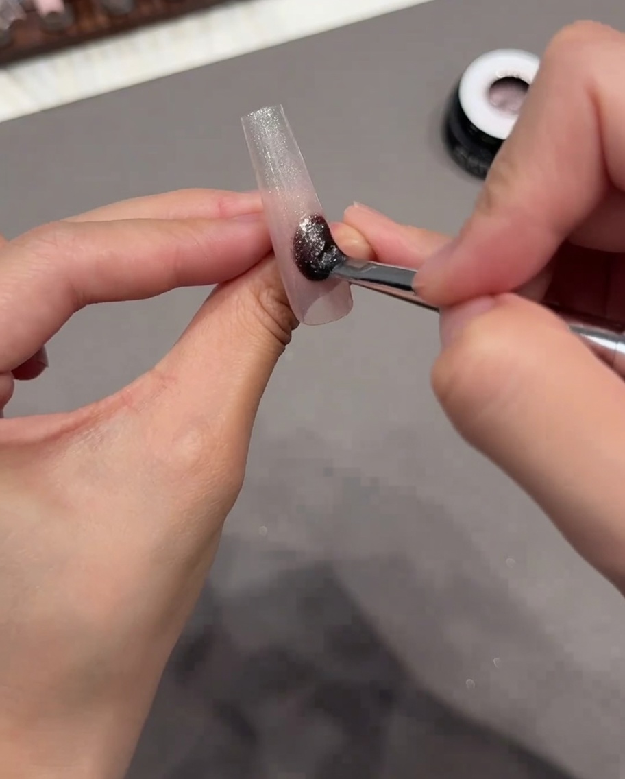 Un pincel aplicando un esmalte de gel ojo de gato brillante sobre toda la superficie de la punta de la uña.